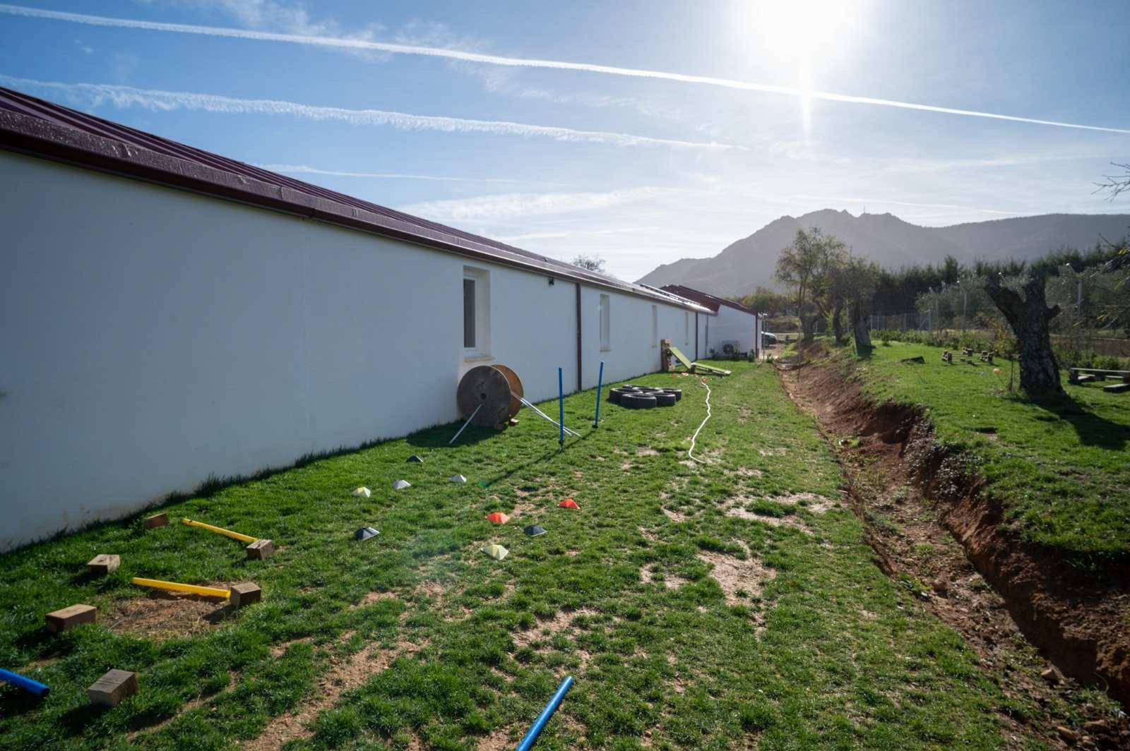 Campo de hierba junto al edificio, preparado con conos y vallas bajas para una sesión de trabajo.